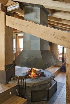 an open fire pit in the middle of a room with wooden floors and beams on either side