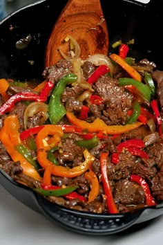 a skillet filled with beef and peppers on top of a table next to a wooden spoon