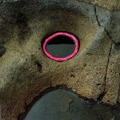 a pink ring sitting in the middle of a rock wall next to a hole that is filled with water