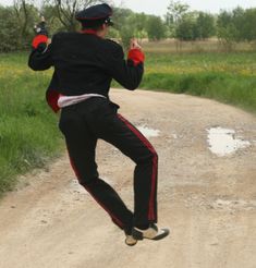 a man is jumping in the air on a dirt road with grass and trees behind him