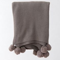 a gray blanket with pom poms hanging from it