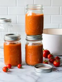 three jars filled with tomato sauce sitting on top of a counter next to some tomatoes