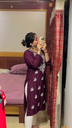 a woman taking a selfie in front of a bed with red curtains and pink bedspread