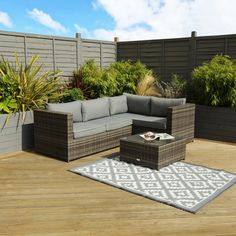 an outdoor living area with couches, tables and rugs on the wooden floor