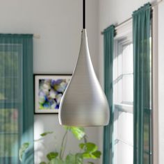 a white hanging light in a living room with green curtains and potted plants on the table