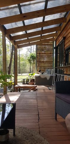 a wooden deck with chairs and tables under a pergolated roof over looking a pond