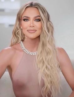 a woman with long blonde hair wearing a halter top and pearls necklace, standing in front of a white background