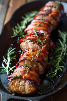 meat wrapped in bacon and garnished with fresh herbs on a black platter