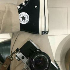 a person holding a camera in their right hand and wearing converse shoes on the other