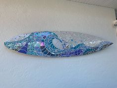 a mosaic glass surfboard hanging on the side of a building with blue and white tiles