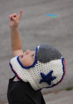 a young boy wearing a crocheted hat and holding his hand up in the air