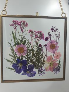 a painting hanging on the wall with flowers painted on it's side and gold chains