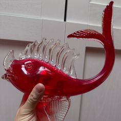 a hand holding a red glass fish figurine in front of a white door