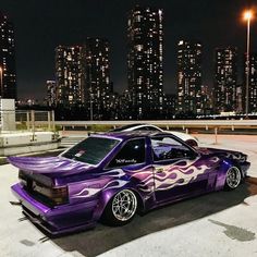 a purple car with flames painted on it parked in front of a city at night