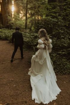 a bride and groom walking through the woods