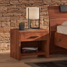 a nightstand with a lamp on it next to a bed and a brick wall behind it