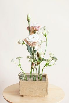 an arrangement of flowers in a square vase on a wooden table against a white wall