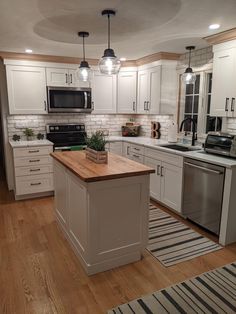 a kitchen with white cabinets and wooden counter tops, an island in the middle is surrounded by striped rugs