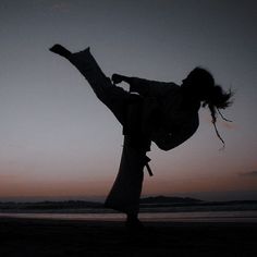 the silhouette of a person doing a kick in front of a body of water at sunset