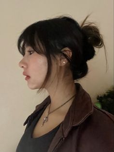 a woman with black hair wearing a brown leather jacket and silver necklace looking off to the side