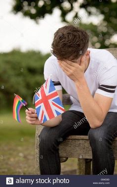 a young man sitting on a bench with his head in his hands and holding a small british flag - stock image