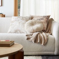 a white couch with pillows on it in front of a window next to a table