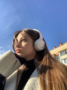 a woman with long hair wearing headphones in front of a building and blue sky