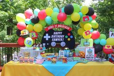 an outdoor birthday party with balloons, cake and snacks on a table in front of a fence