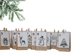 a row of christmas cards with drawings on them hanging from clothes pegs in front of a pine tree