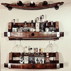 two wooden shelves filled with liquor bottles and glasses on top of each other in front of a white wall