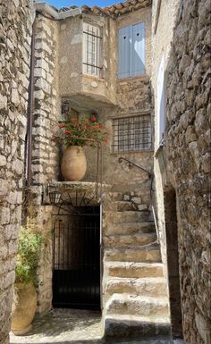 an old stone building with stairs leading up to the door and flowers in pots on the ledge