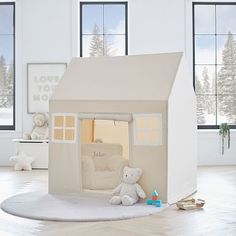 a white teddy bear sitting in front of a house shaped like a doll's house