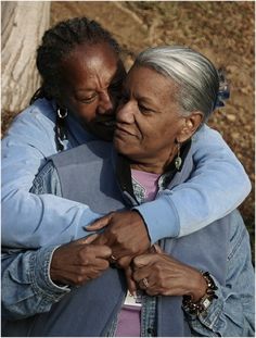 two women embracing each other in front of a tree