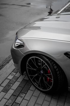 the front end of a silver car parked on a brick road next to a parking meter