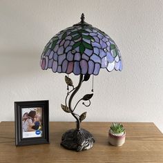 a lamp sitting on top of a wooden table next to a potted plant and a framed photo