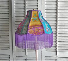 a lamp that is on top of a wooden pole with fringes around the lampshade