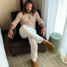 a man with long hair sitting in a chair next to a small round foot stool