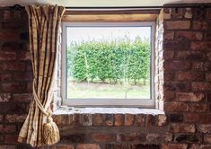 a brick wall with a window and curtain on it's side, in front of a tree