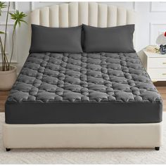 an image of a bed that is in the room with grey sheets and pillows on it