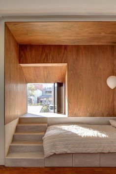 a bed sitting under a window in a bedroom next to a wooden wall and stairs