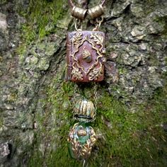 two necklaces are attached to a tree trunk with moss growing on it and hanging from chains