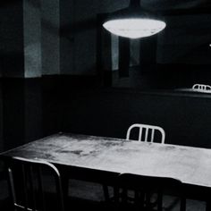 an empty table and chairs in a dark room with lights on the ceiling above it