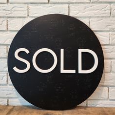 a black and white sign that says sold on the side of a brick wall in front of a wooden table