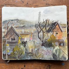 an open book with watercolors on it sitting on top of a wooden table