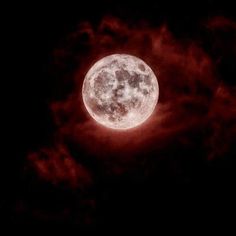 the full moon is seen through clouds on a dark night with red light coming from it