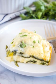 a white plate topped with lasagna covered in cheese and green vegetables next to a fork