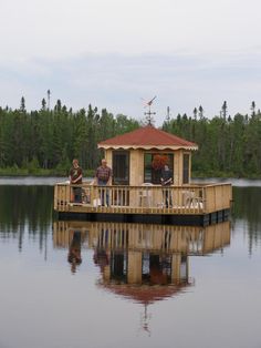 three people are standing on the deck of a houseboat that is floating in a lake