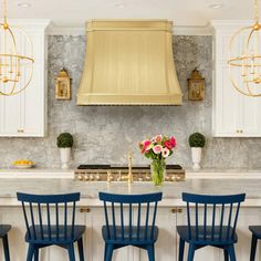 four blue chairs are in front of a kitchen island with gold range hood above it