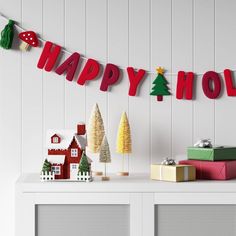 christmas decorations and presents on a shelf in front of a happy holidays banner hanging from the wall