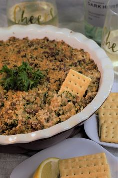 a casserole dish with crackers, lemon wedges and parsley on the side